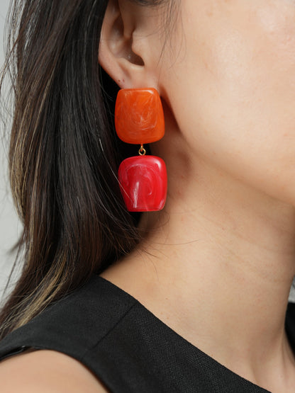 Close-up of a person wearing red square earrings with a neutral background