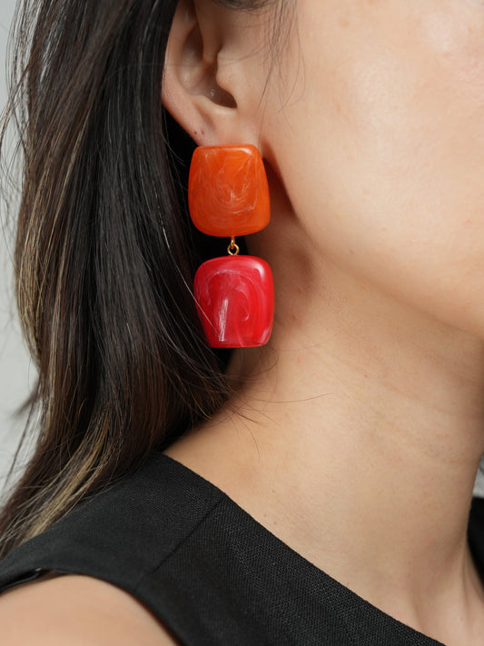 Close-up of a person wearing red square earrings with a neutral background