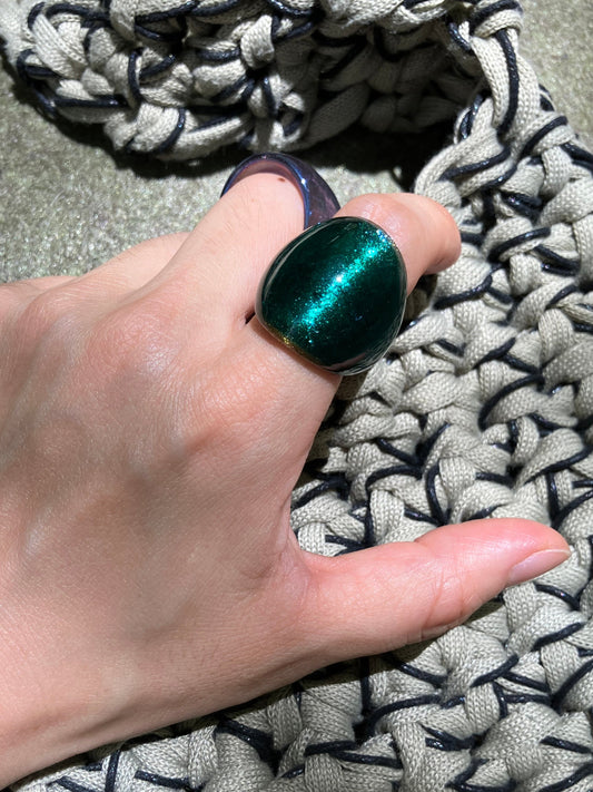 Hand wearing a green metallic ring on a textured surface